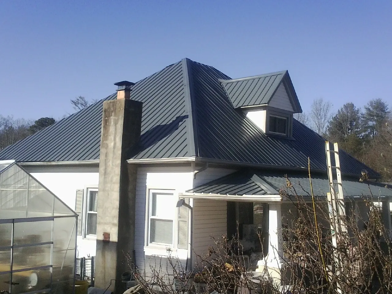 Dark blue standing seam metal roof on a white farmhouse with dormer — Slate & Tile Roof Repair by Roofing Brothers in Olaton