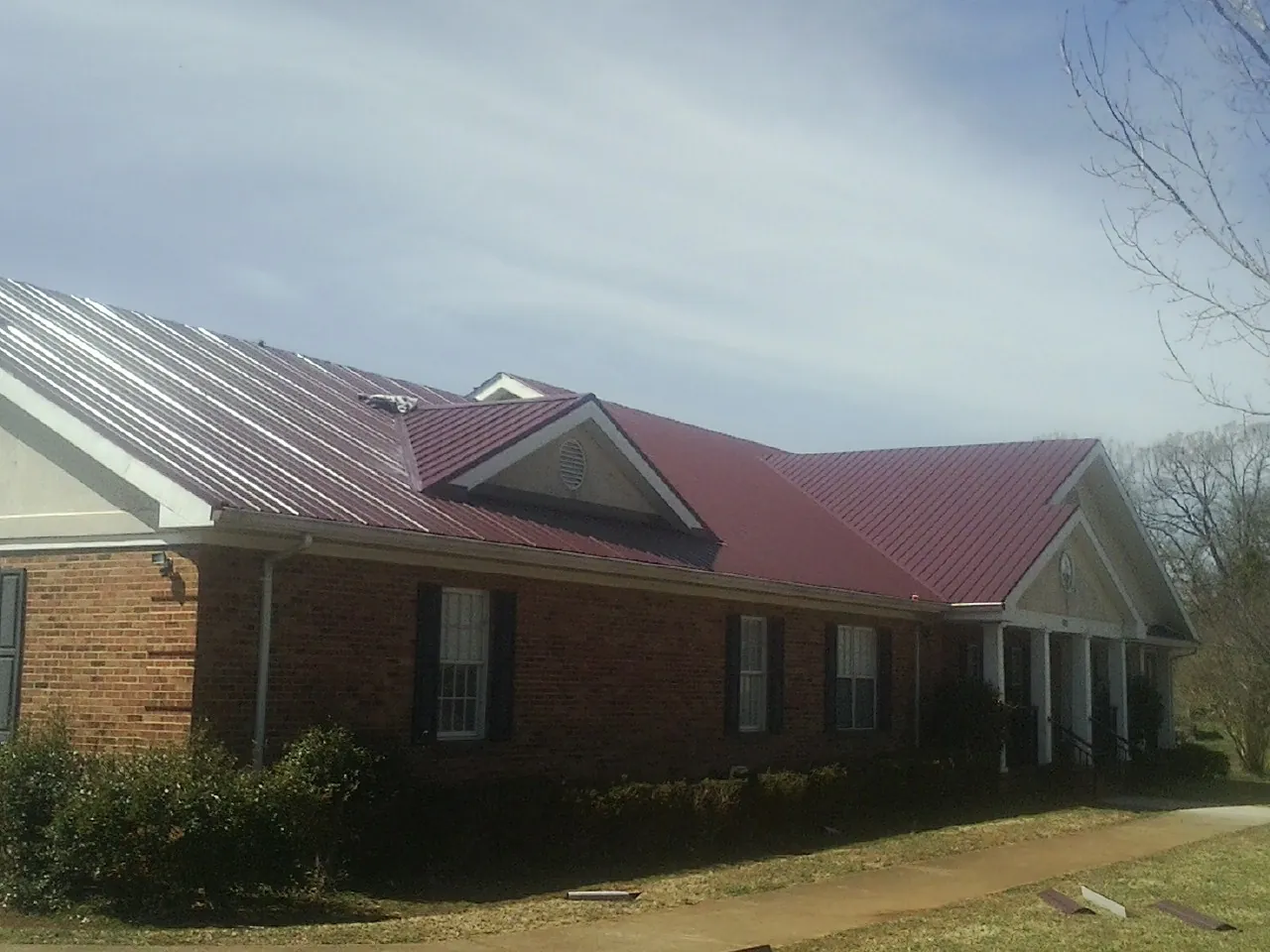 Red metal roof with gabled entries on a long brick building, from a Hail Damage Roof Repair job in Olaton