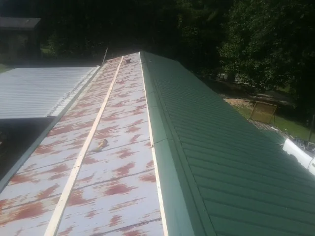 Old rusted panels beside newly installed green metal roofing — Wind Damage Roof Repair by Roofing Brothers in Olaton