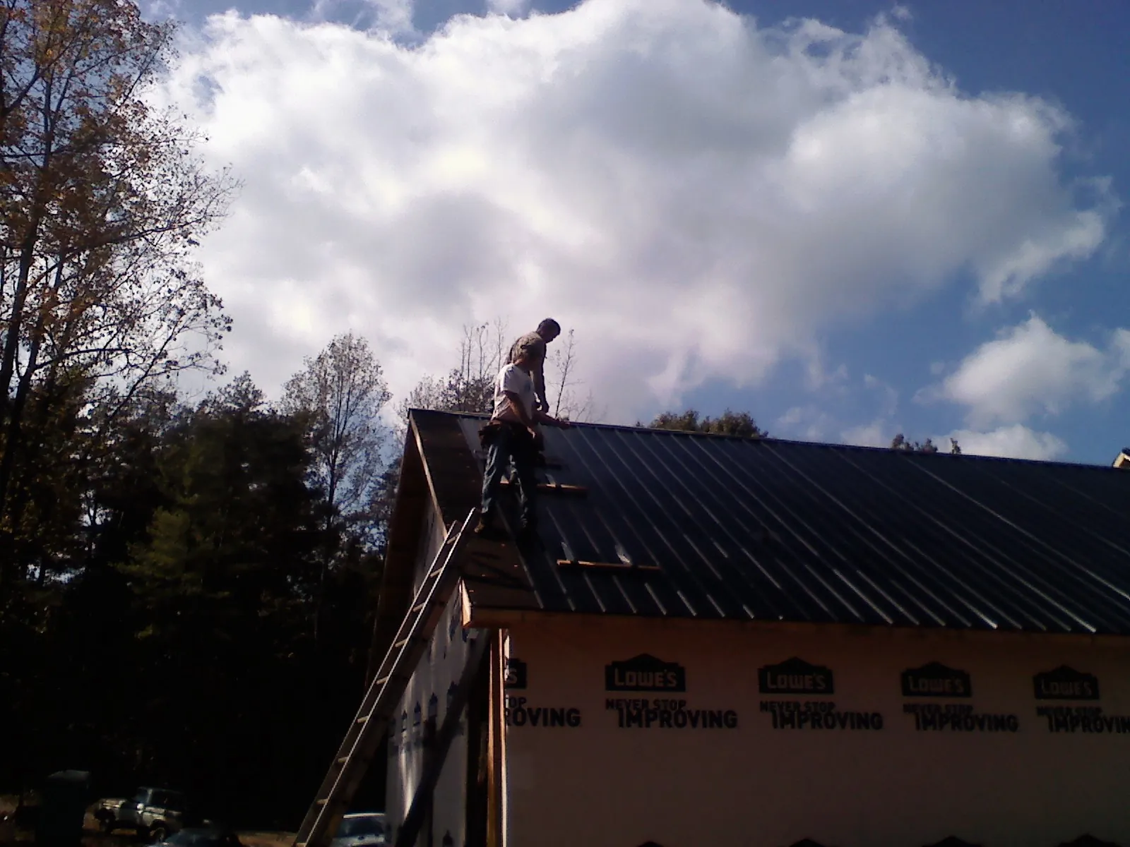 Roofer fastening dark metal panels high against a cloudy sky, from a Roof Inspection job in Olaton