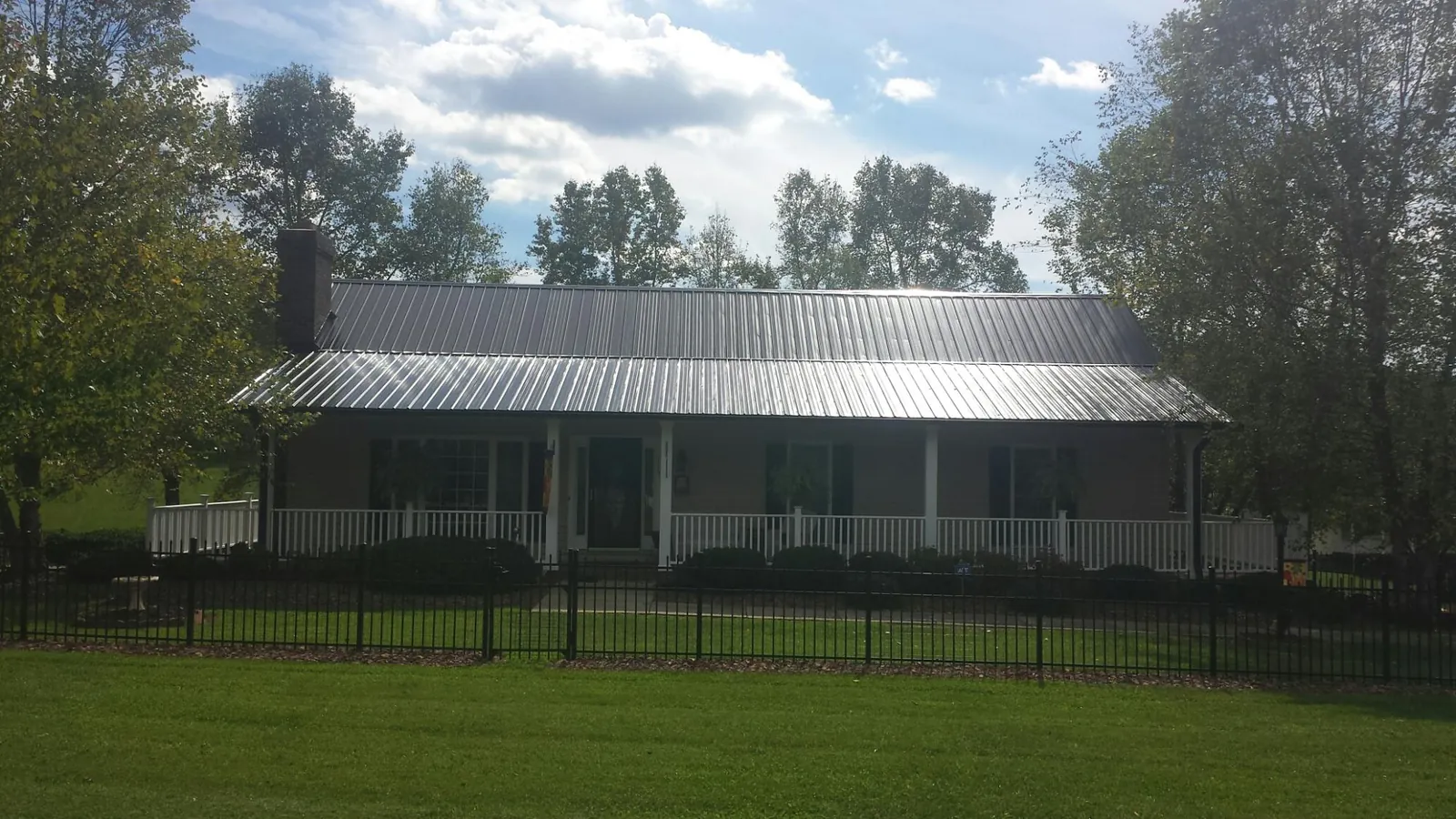 Gray metal roof on a brick ranch with a full width front porch — Gutter Guard Installation work by our crew in Olaton