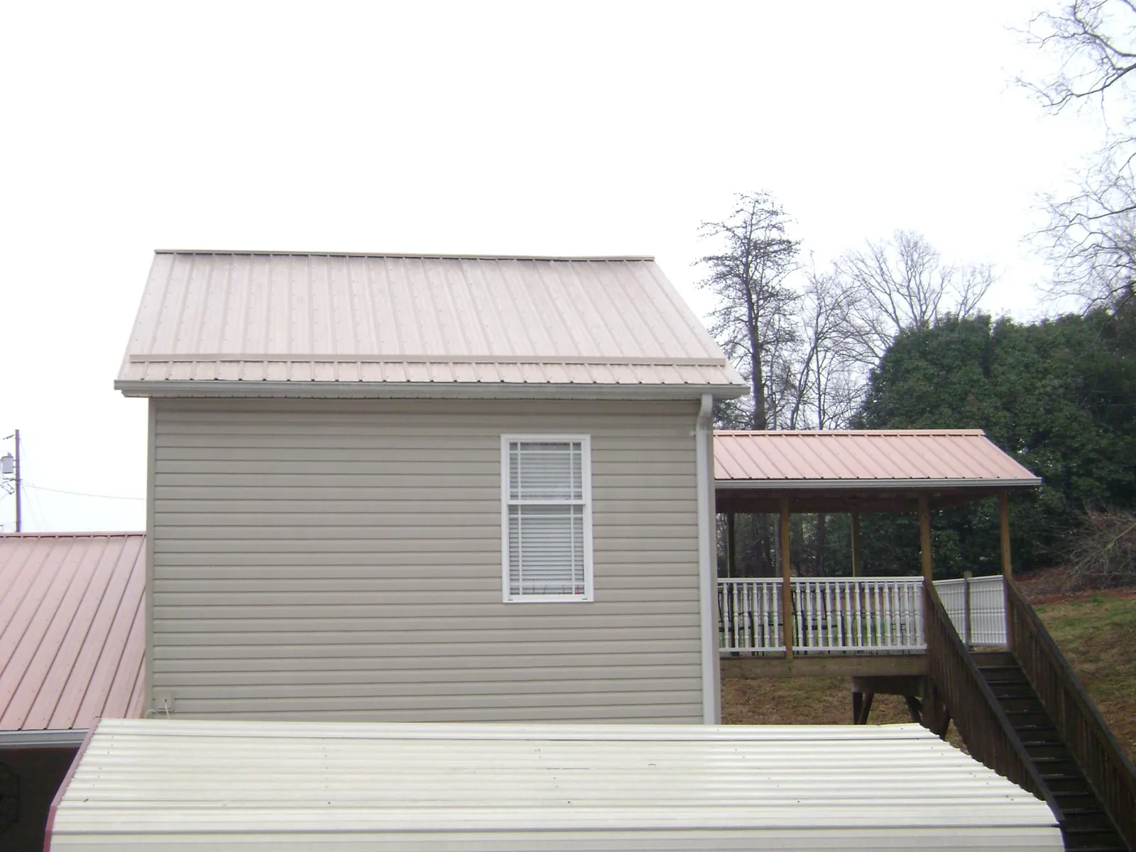 Tan metal roofs on a two story addition and attached porch, from a Roof Replacement job in Olaton